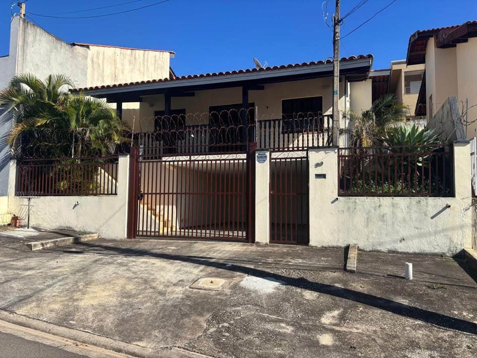 Fachada de casa térrea com muro baixo, portão de ferro marrom e cerca elétrica.