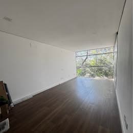 Salão comercial amplo com piso amadeirado, paredes brancas e grande janela com vista para vegetação.