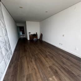 Salão comercial amplo com piso amadeirado, paredes brancas e detalhe de revestimento na parede lateral.