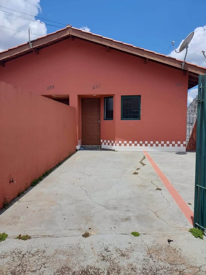 Fachada de casa térrea com pintura rosa, porta de madeira e piso de cimento na entrada.