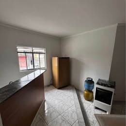 Cozinha compacta com piso em cerâmica branca, pia com bancada em L, geladeira marrom e fogão com botijão de gás.