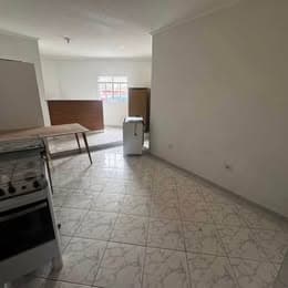 Ambiente integrado amplo com piso em cerâmica clara, paredes brancas, janela e móveis soltos.